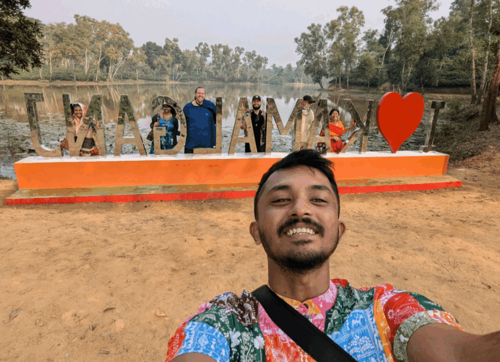 A traveler taking a selfie in front of the decorative "I Love Madhabpur" landmark at Madhabpur Lake in Sreemangal, Bangladesh.