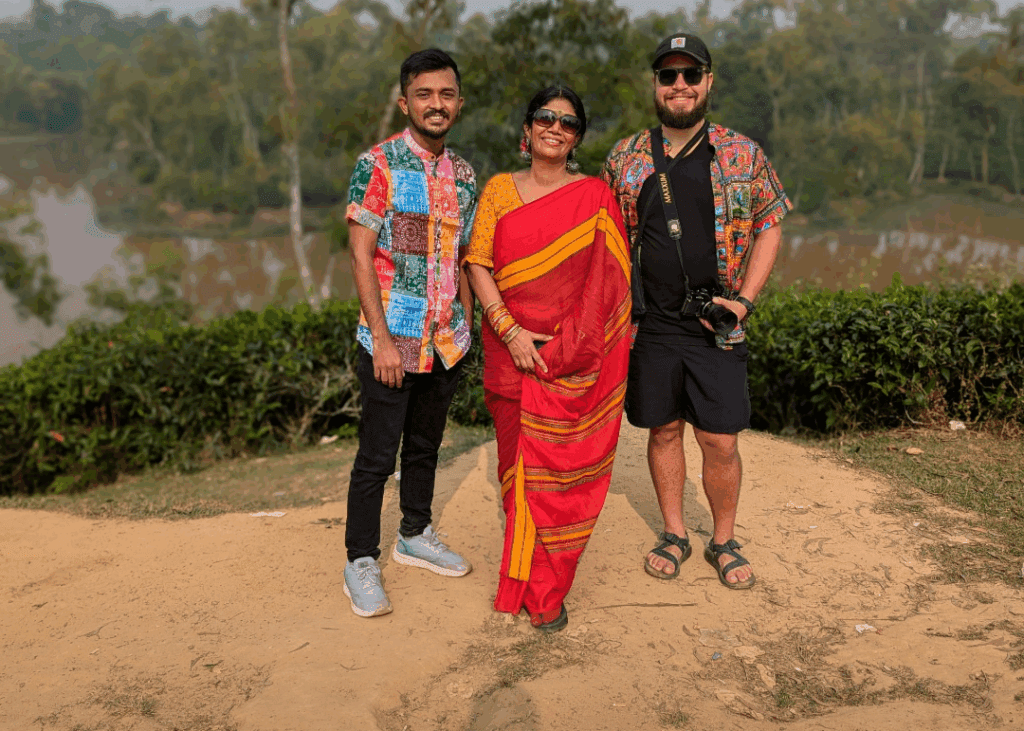 A group of international travelers and a local guide in traditional attire standing in the scenic tea gardens of Sreemangal, Bangladesh, during a TripGlider tour.