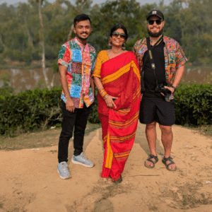 A group of international travelers and a local guide in traditional attire standing in the scenic tea gardens of Sreemangal, Bangladesh, during a TripGlider tour.