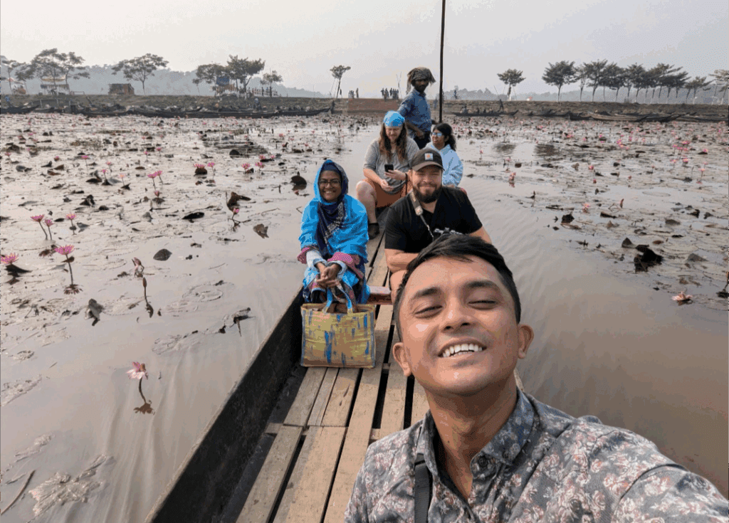 Travelers and a guide on a wooden boat navigating through a marsh filled with blooming water lilies in Sylhet.