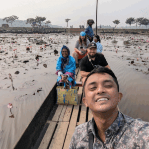 Travelers and a guide on a wooden boat navigating through a marsh filled with blooming water lilies in Sylhet.