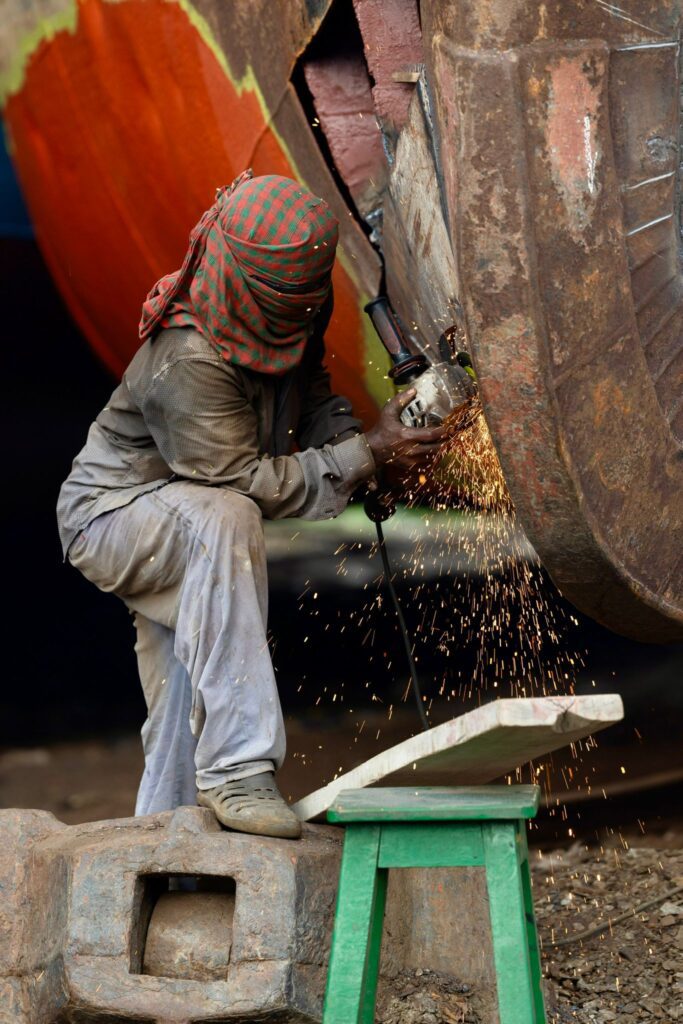 A worker wearing protective gear using a blowtorch to cut through a massive metal ship hull at a shipbreaking yard in Chittagong, Bangladesh.